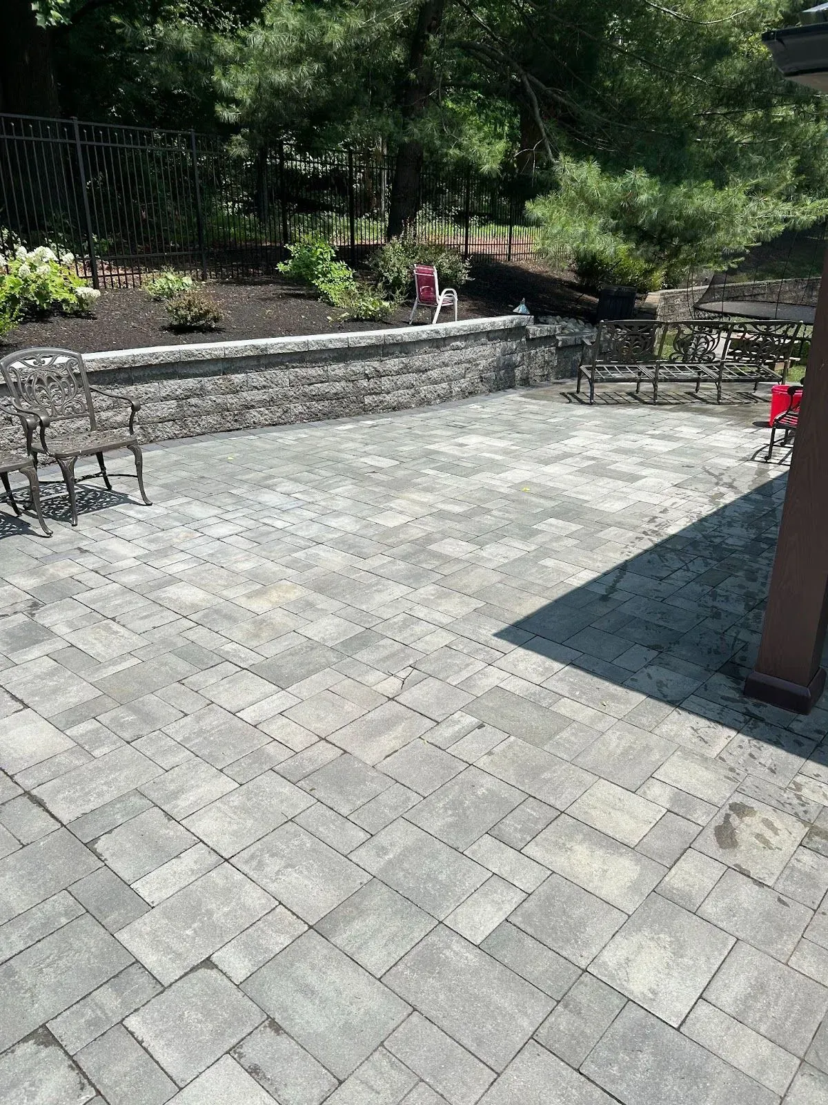 A brick patio with chairs and a fence in the background.