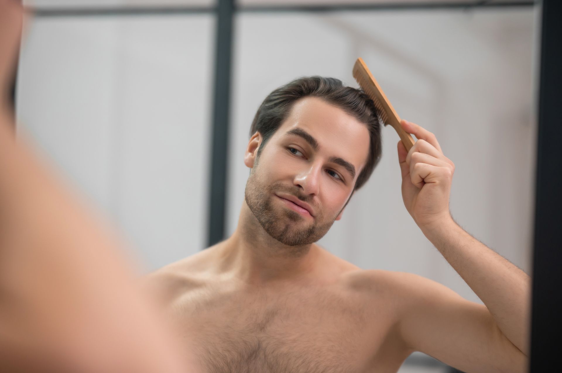 a shirtless man is brushing his hair in front of a mirror .