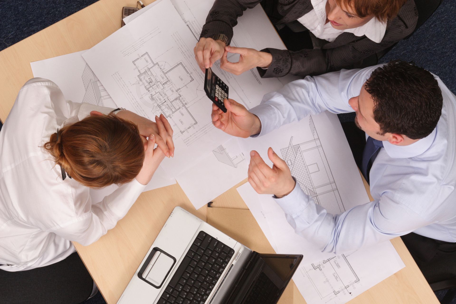 A group of people are sitting around a table looking at a blueprint