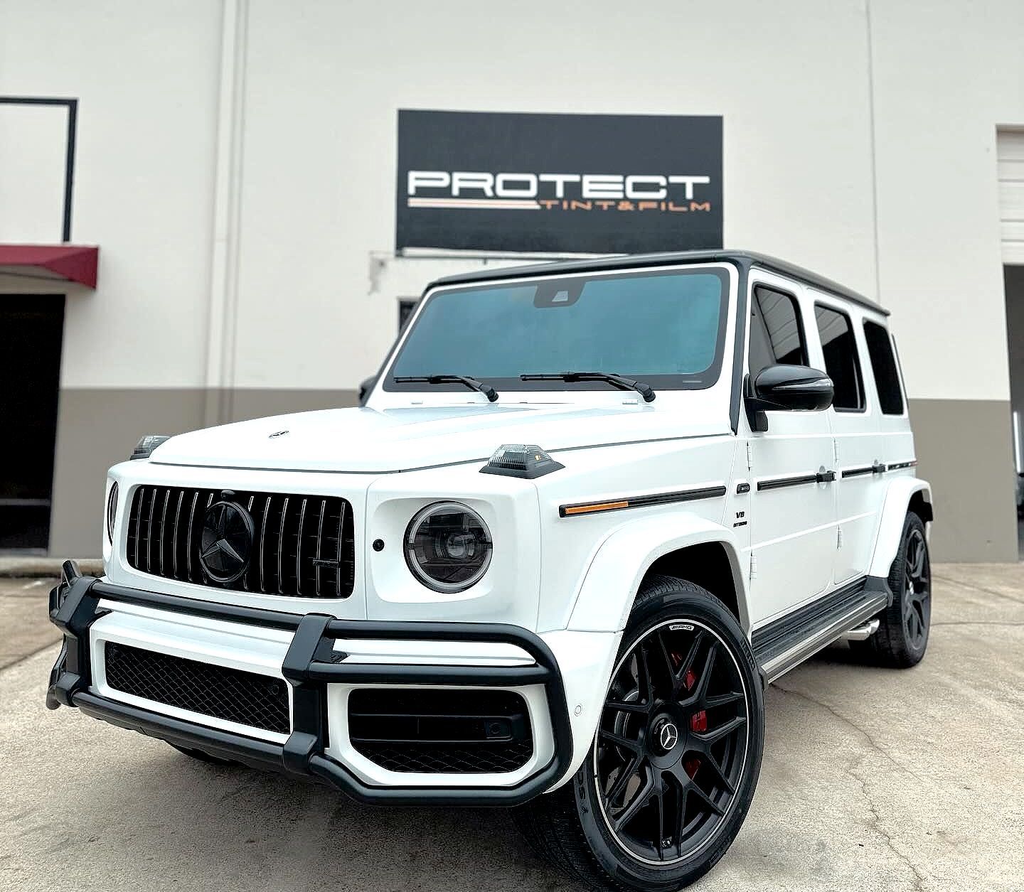 A white jeep is parked in front of a building that says protect