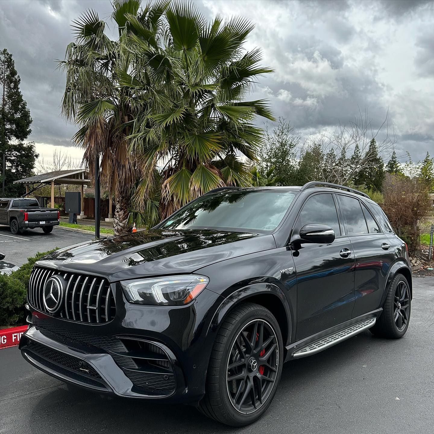 A black mercedes benz gle suv is parked in a parking lot with palm trees in the background.