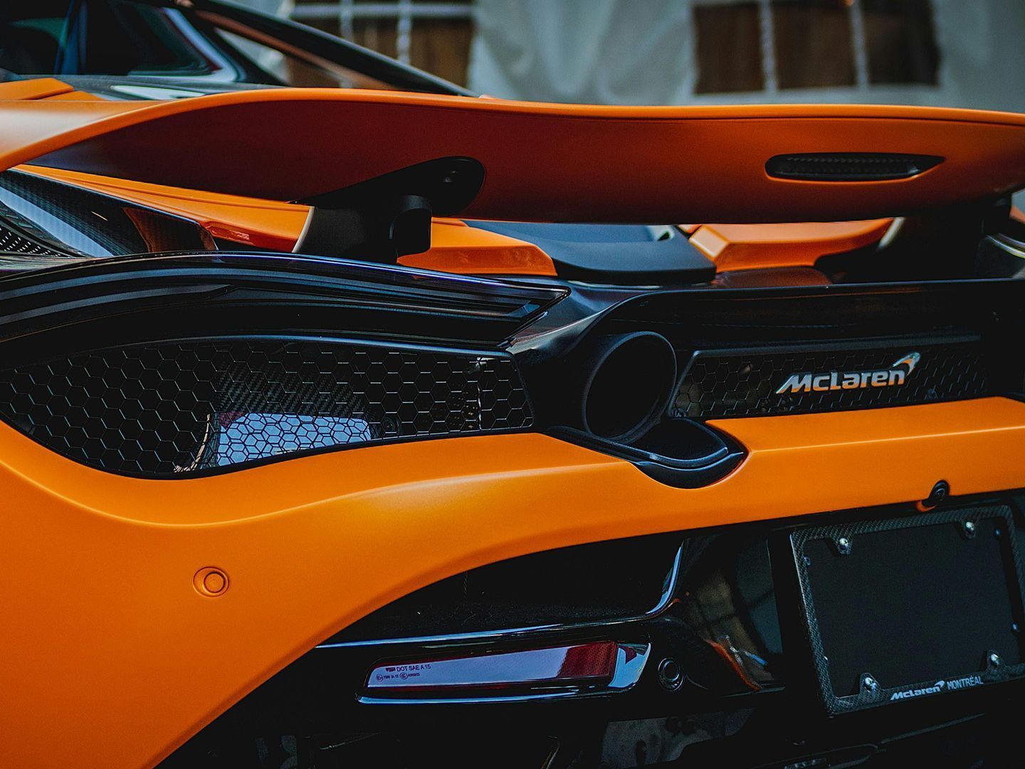 An orange sports car is parked in front of a palm tree.