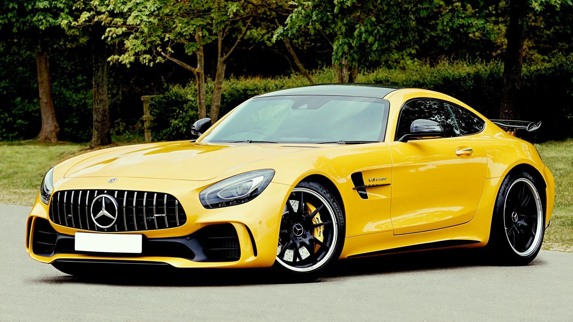 Yellow Mercedes-AMG GT R coupe parked on a paved road, set against a backdrop of trees.