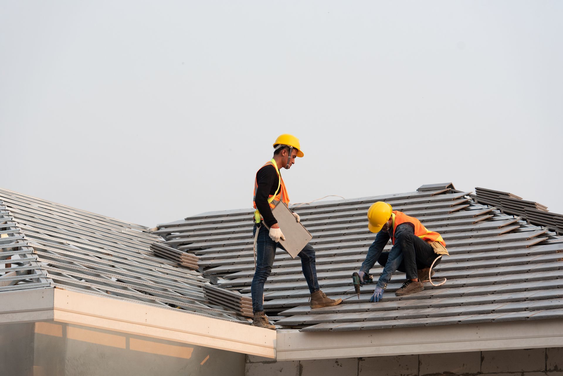 Two construction workers are working on the roof of a building.