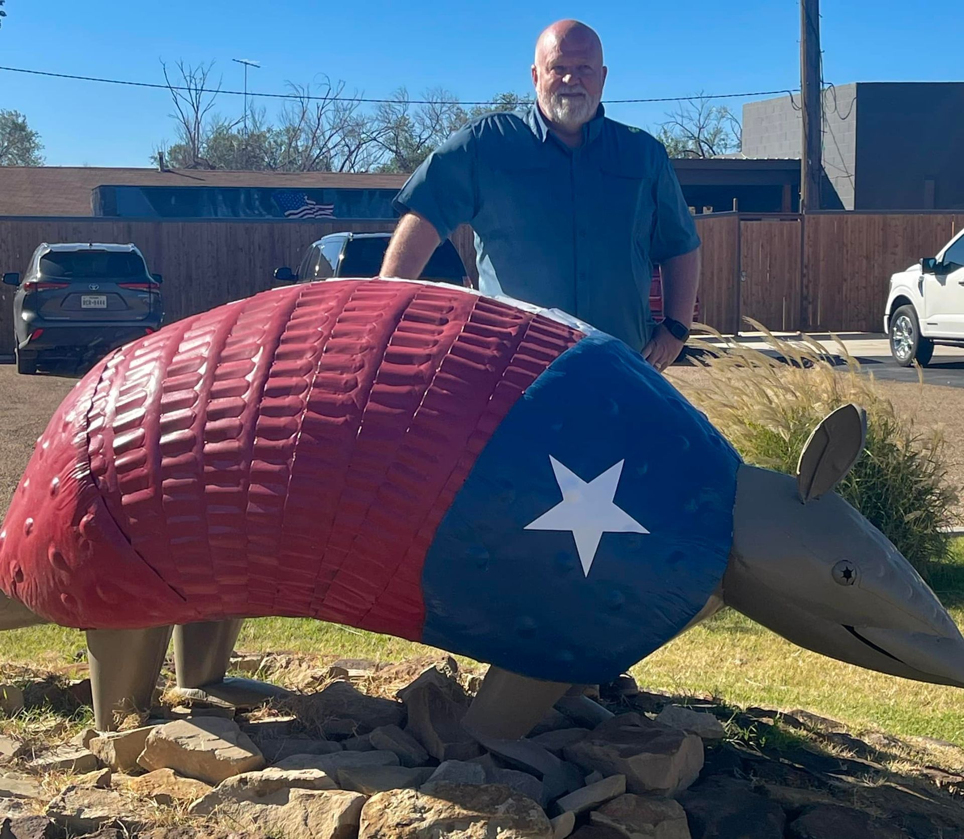 Man standing behind a large red, blue, and silver armadillo sculpture outdoors