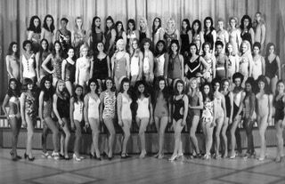 Large group of dancers posing on a stage in front of curtains, in black-and-white.