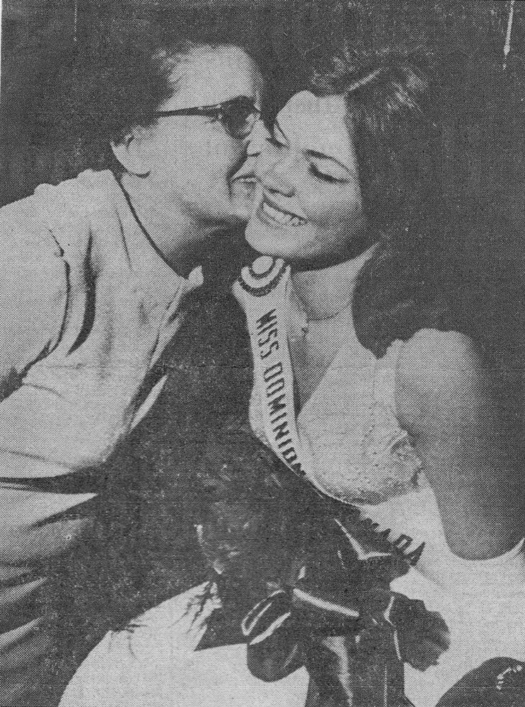 Person kissing a smiling pageant winner holding flowers and wearing a sash and crown