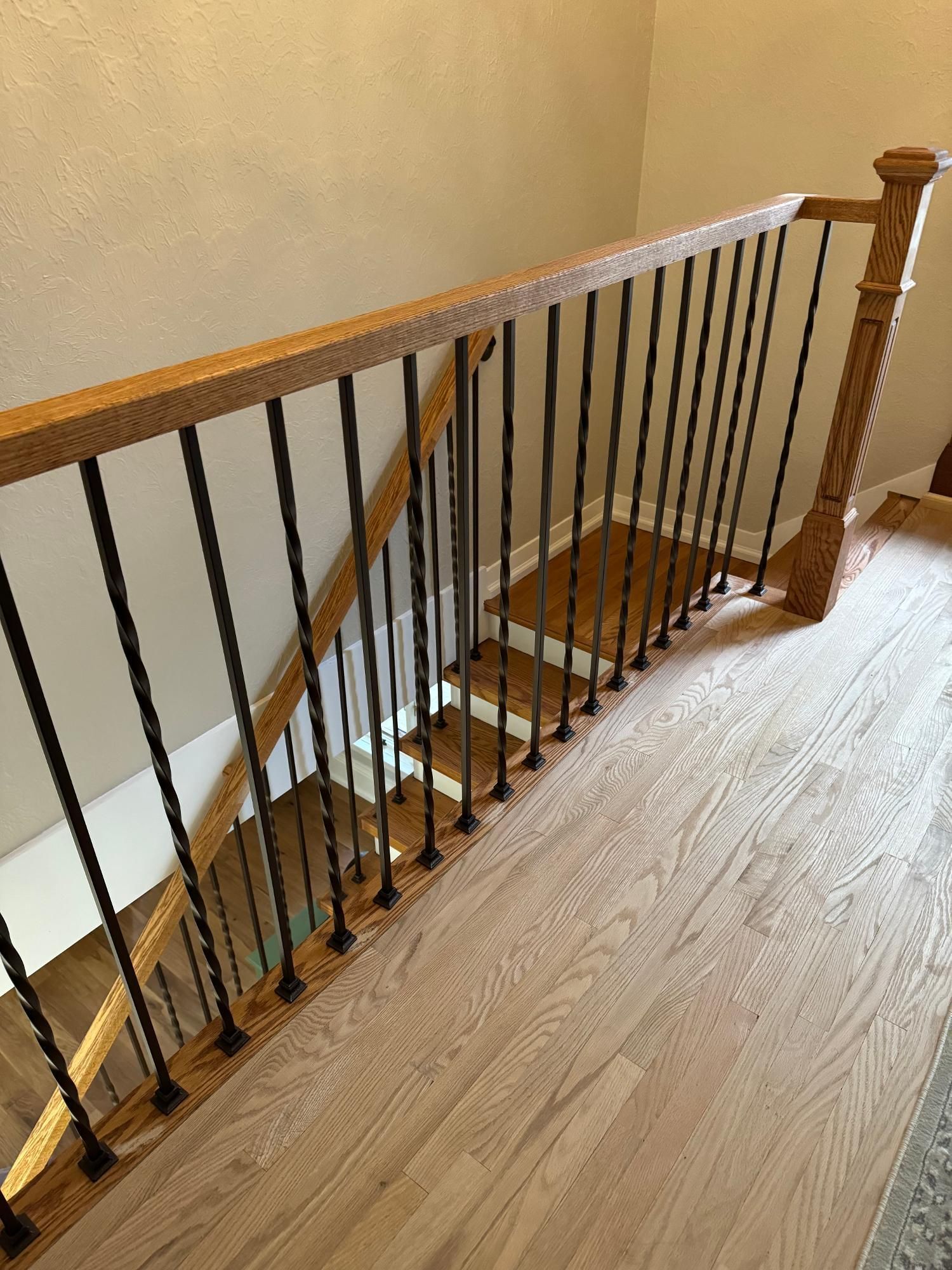 A wooden staircase with a handrail and dark metal vertical balusters overlooking a lower level.