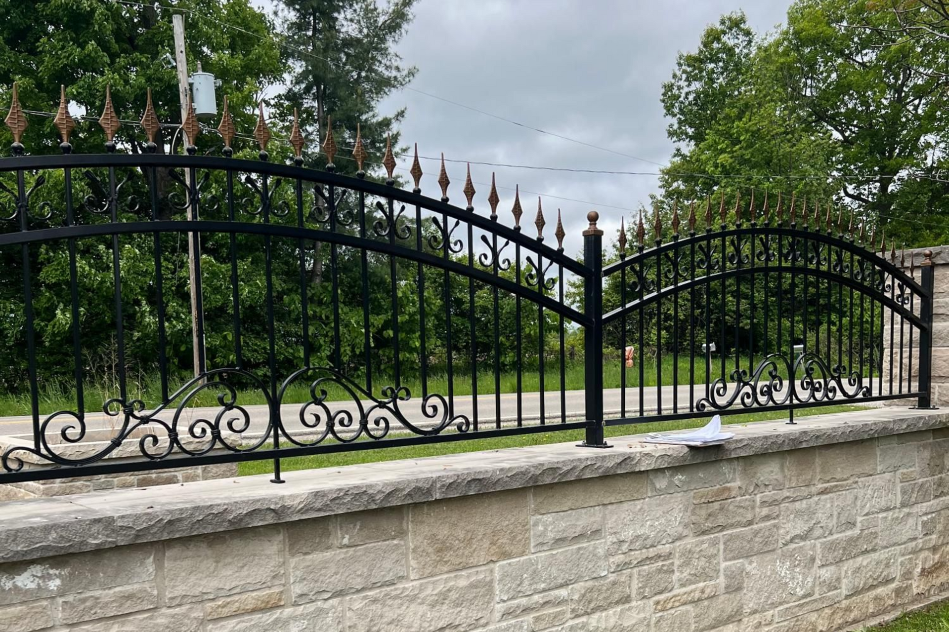A decorative black wrought iron fence with arched tops and gold-tipped finials sits atop a light stone wall.