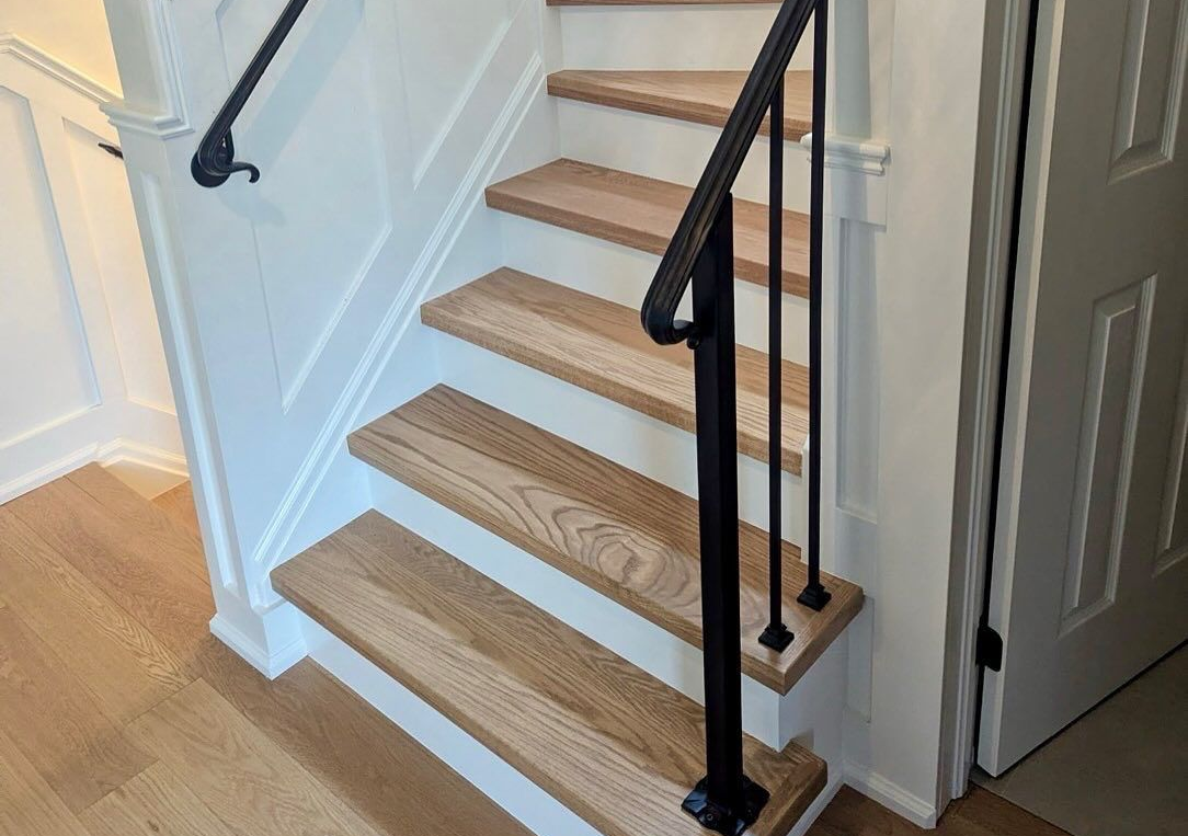 A wooden staircase with white risers and black metal railings ascending along a white wall.