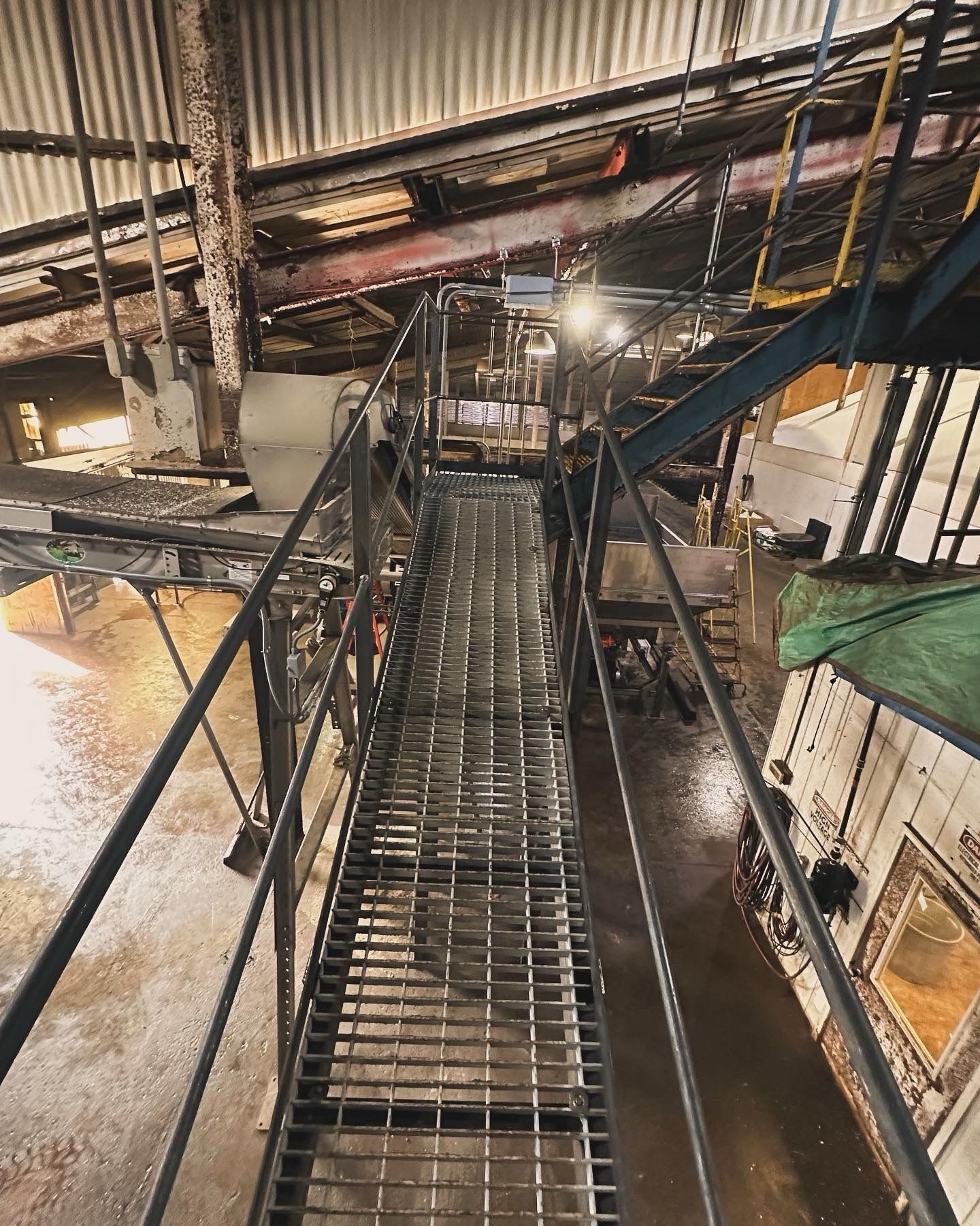 Metal catwalk in industrial setting, stairs, pipes, and machinery visible.