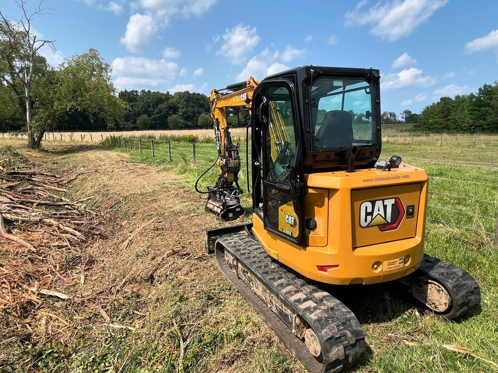 Yellow Caterpillar mini excavator clearing a field under a blue sky.