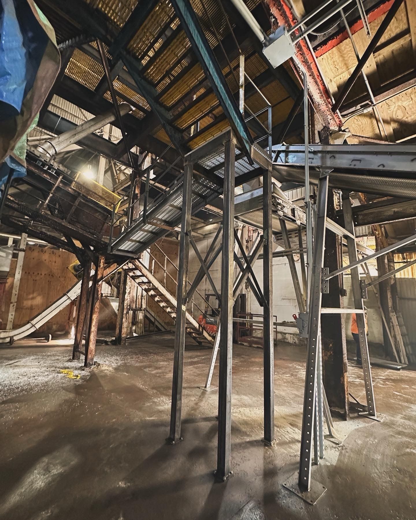Interior view of a industrial building with metal structures, stairs, and wet floor.