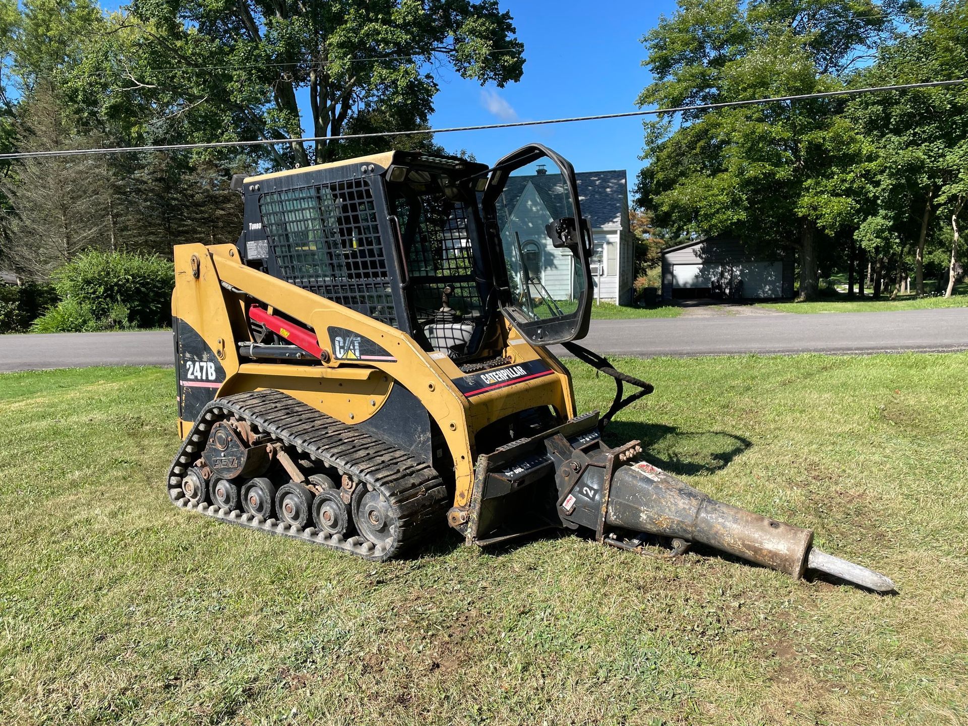 A bulldozer with a hammer attached to it is parked in a grassy field.