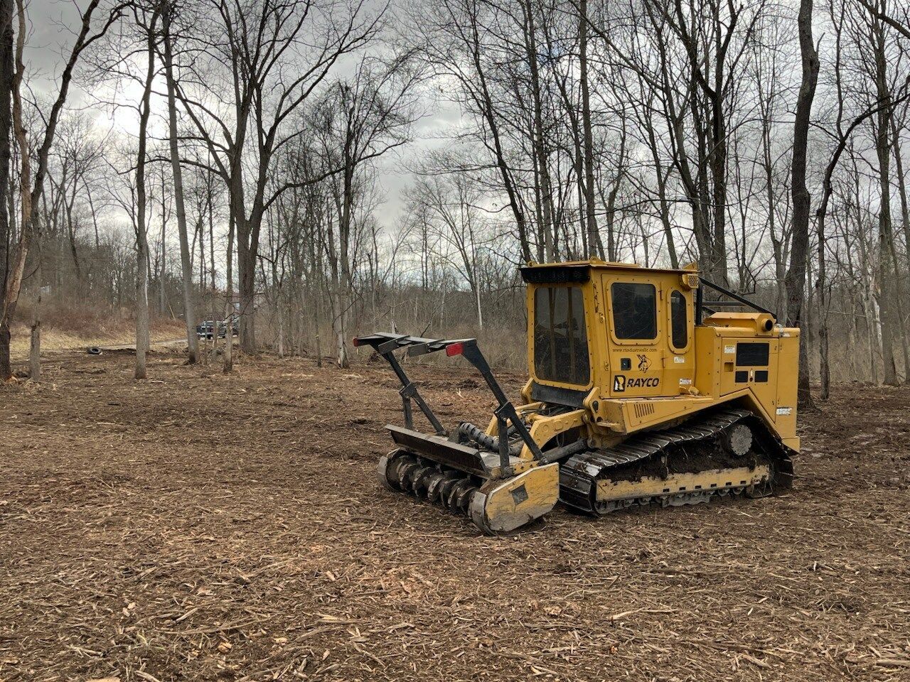 Yellow forestry mulcher clearing wood chips in a forest.