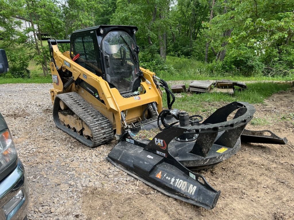 Yellow skid steer with brush cutter attachment outdoors.