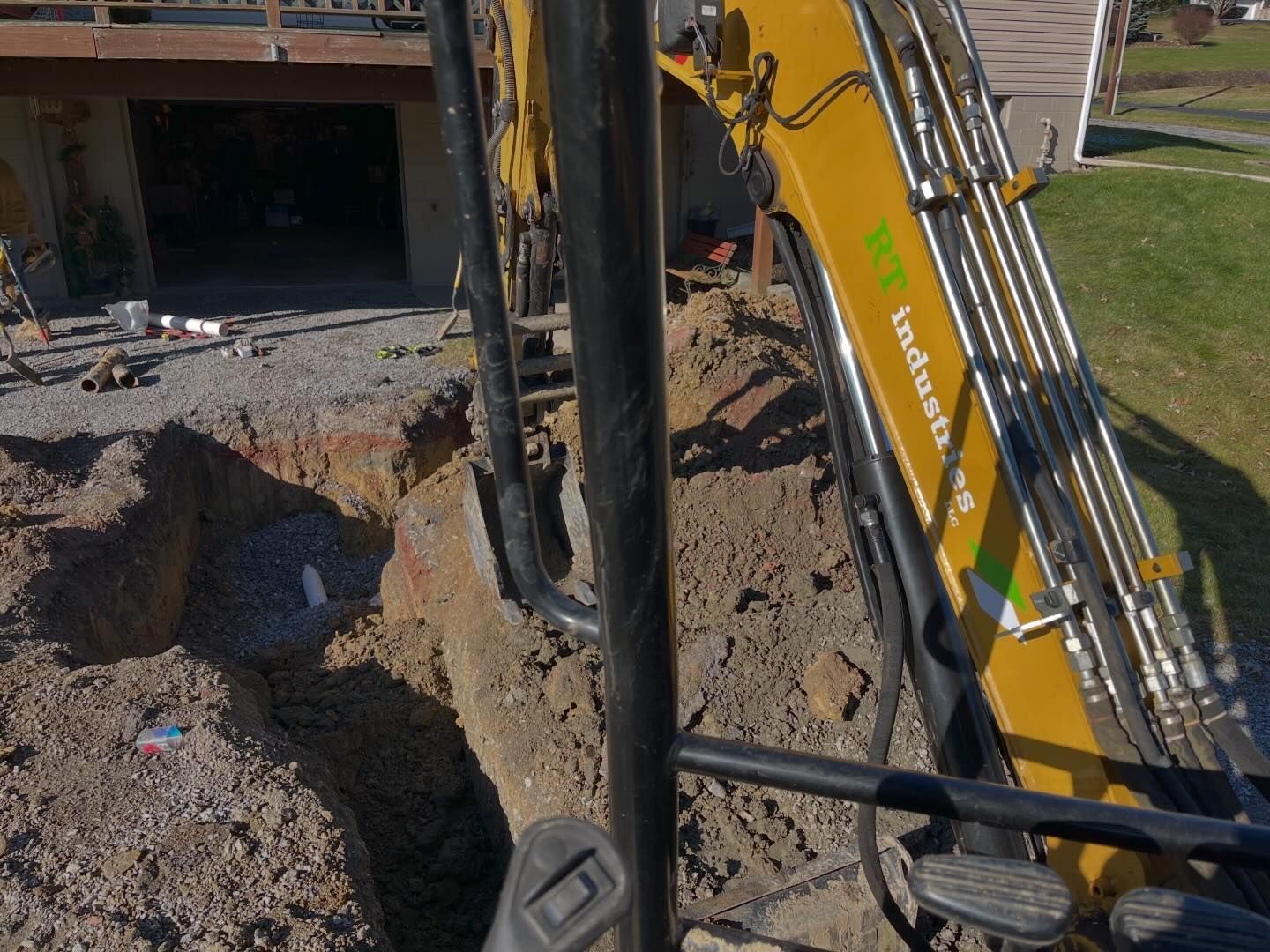 A yellow excavator is digging a hole in the dirt in front of a house