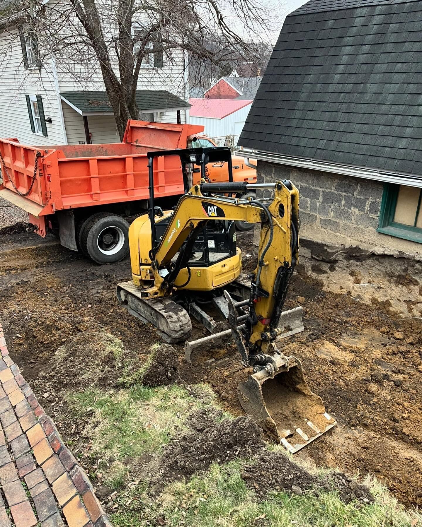 A small excavator is digging a hole in front of a dump truck.