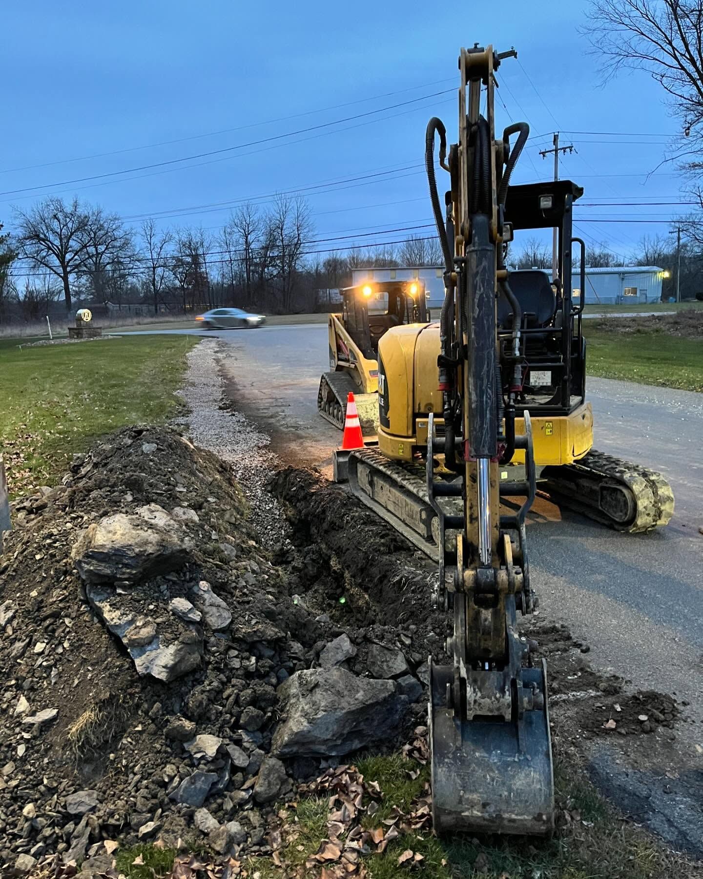 A yellow excavator is digging a hole on the side of a road.
