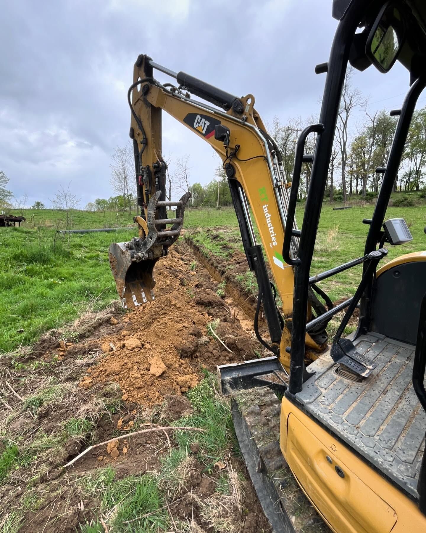 A yellow excavator is digging a hole in a field.