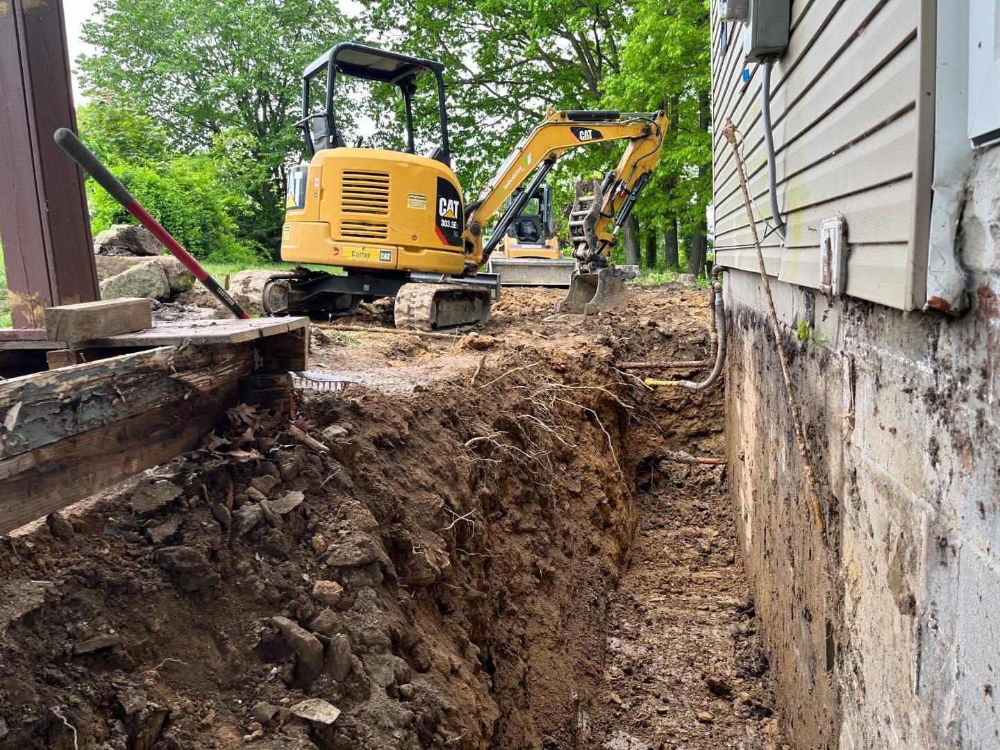 A yellow excavator is digging a hole in front of a house.