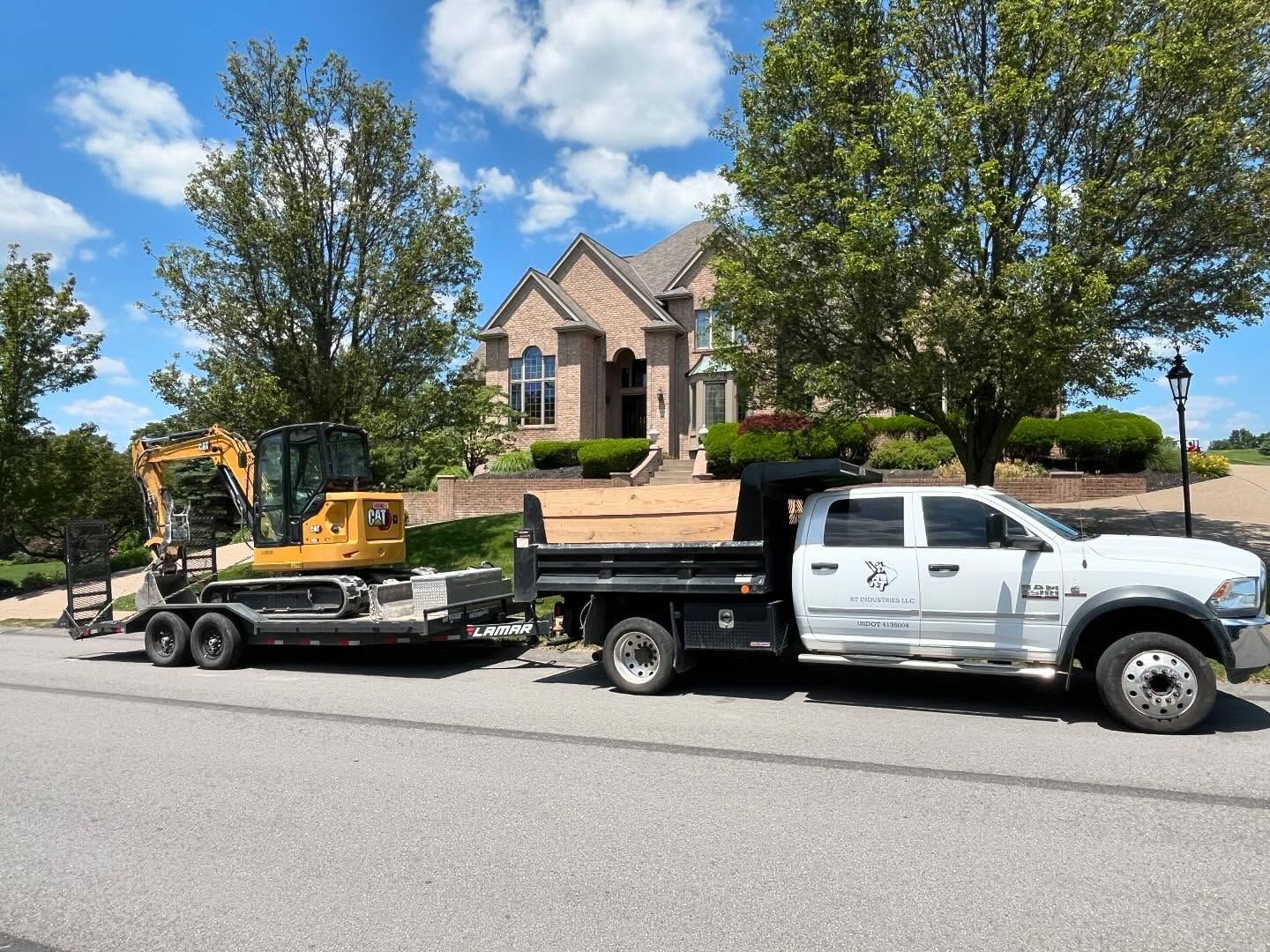A dump truck is towing an excavator on a trailer.