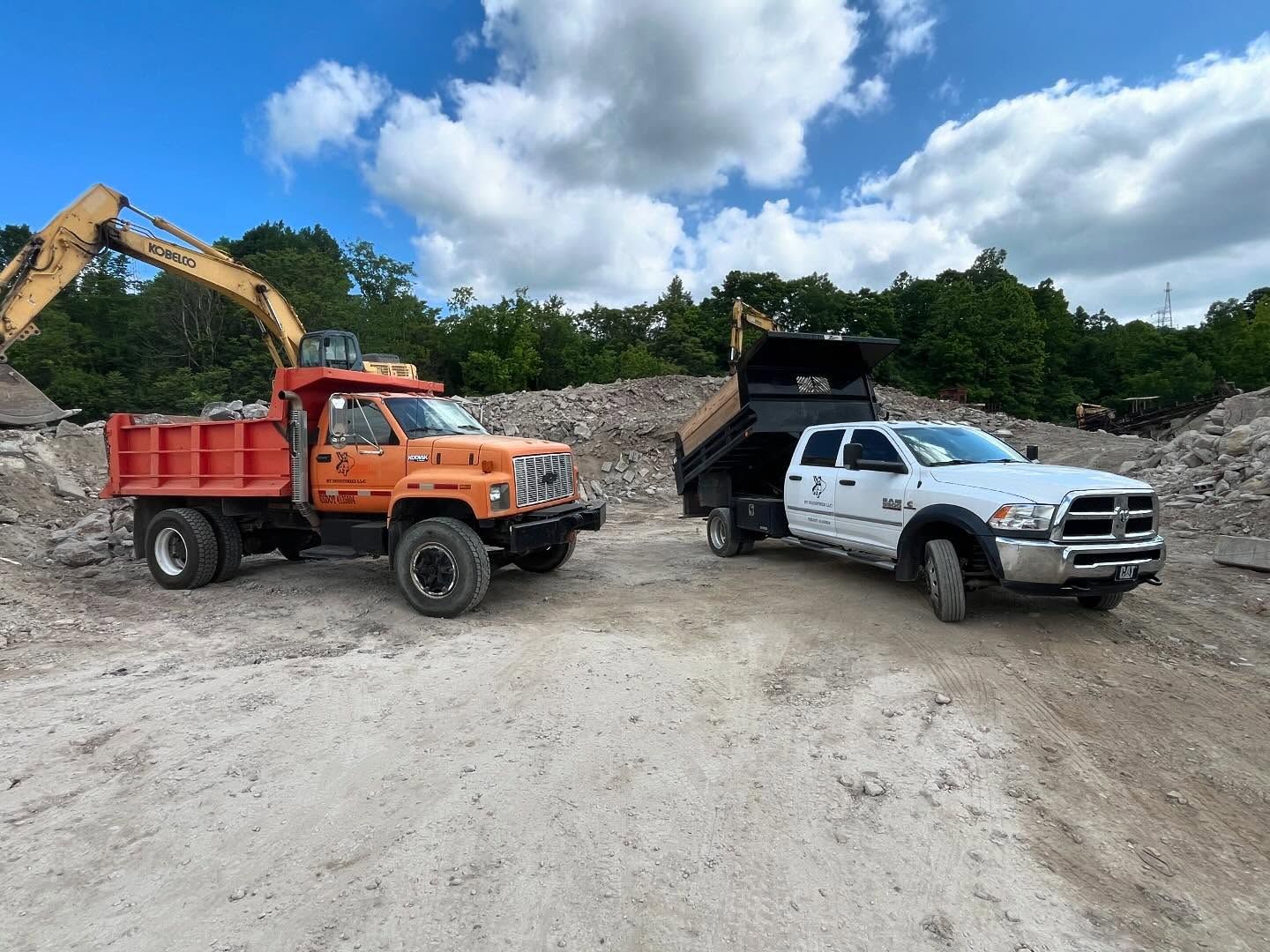Two dump trucks are parked next to each other in a dirt field.