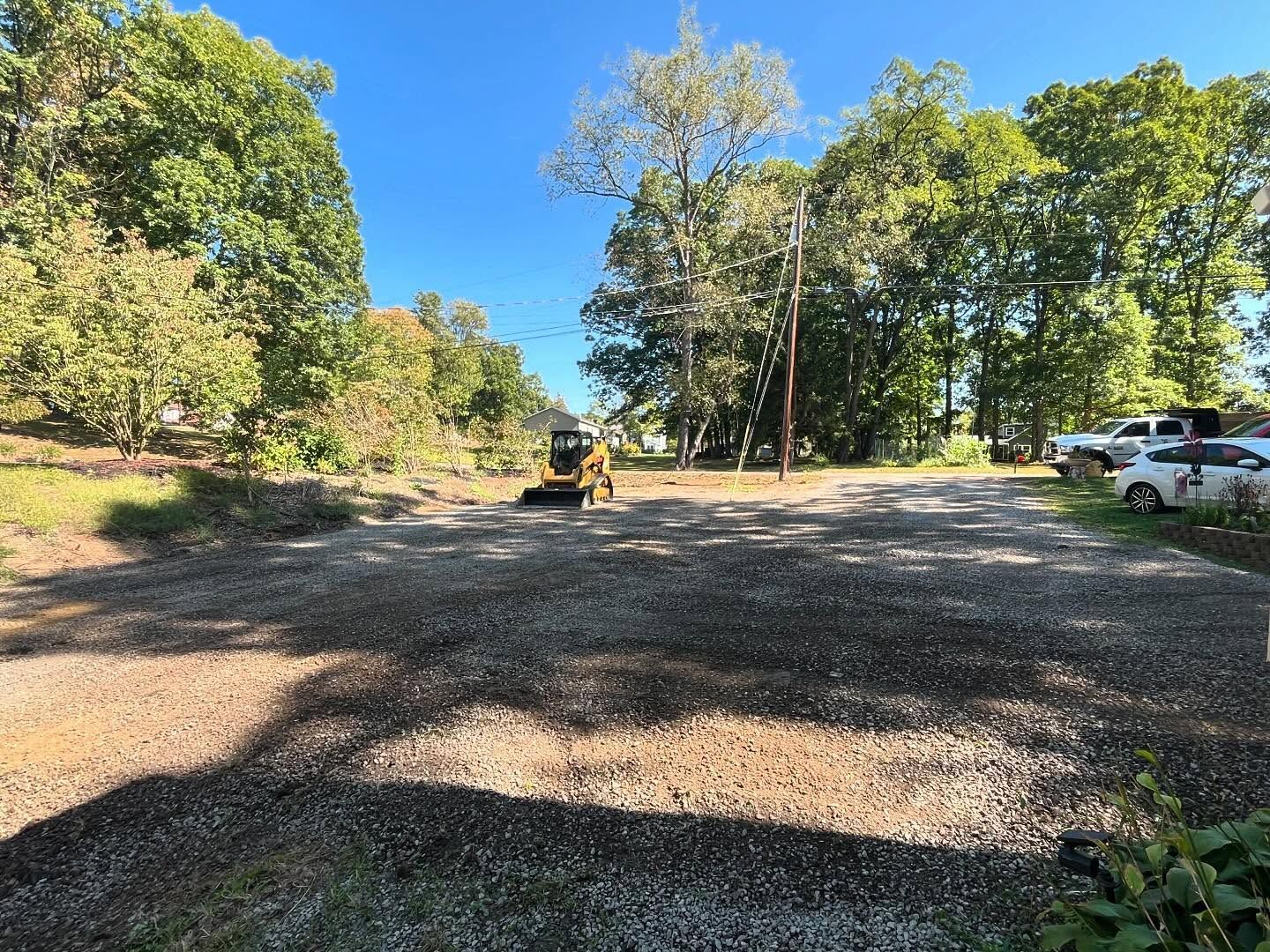 A bulldozer is driving down a gravel road surrounded by trees.