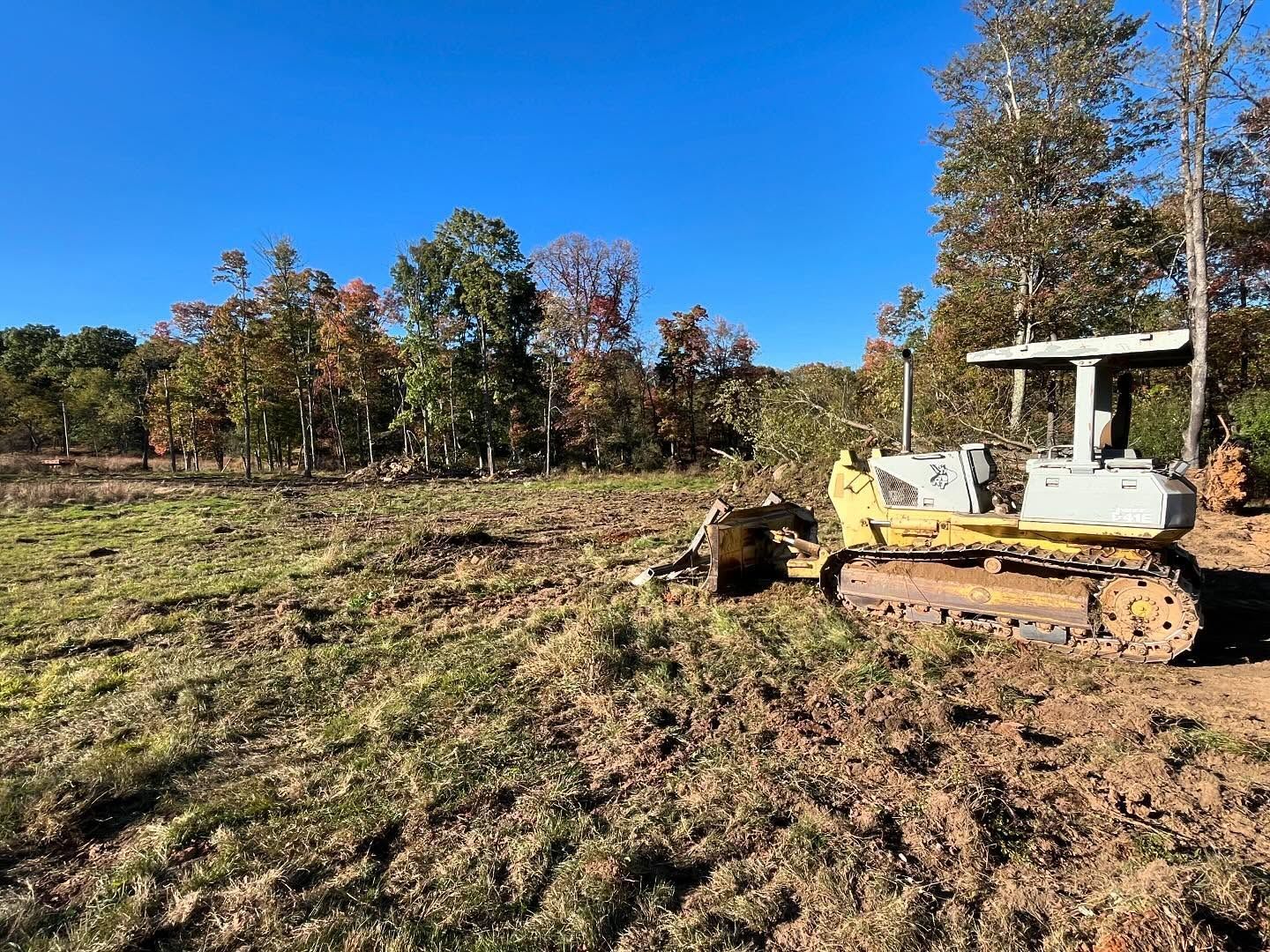 A bulldozer is plowing a field with trees in the background.