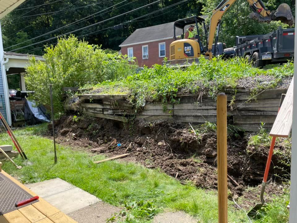 An excavator is digging a hole in a yard next to a house.