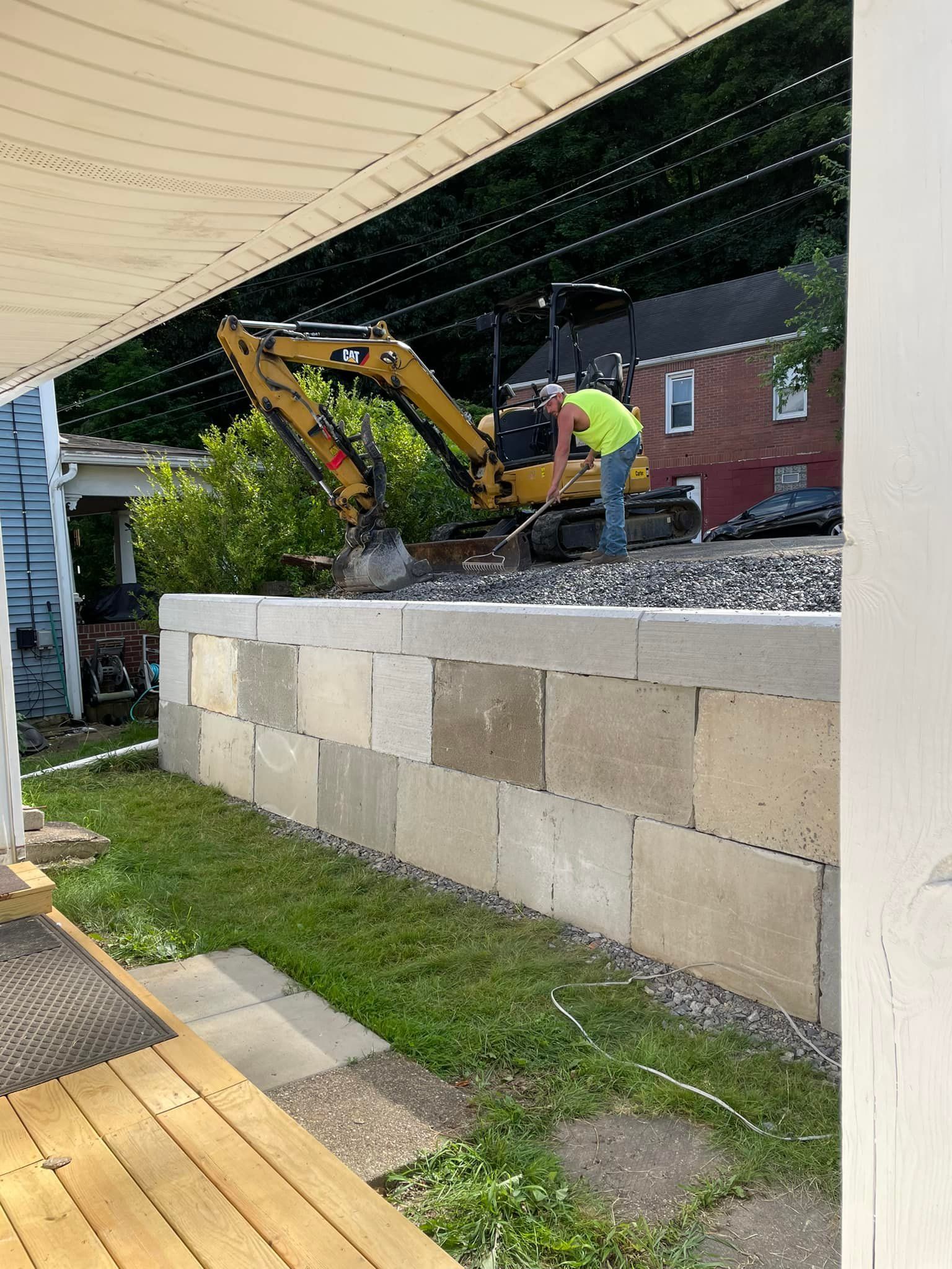 A man is working on a brick wall with a yellow excavator in the background.