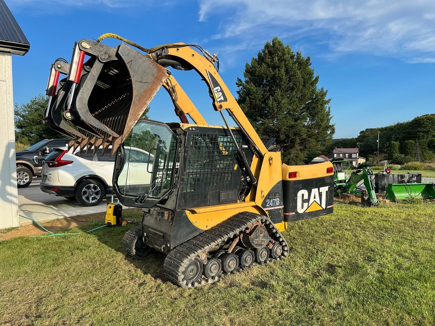 A cat skid steer loader is parked in a grassy field.