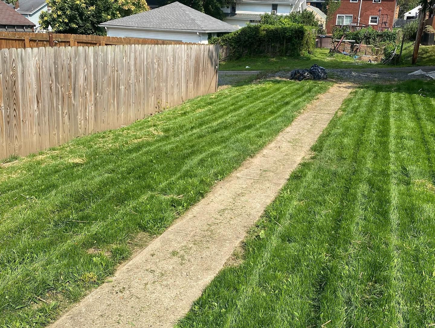A path going through a lush green lawn next to a wooden fence.