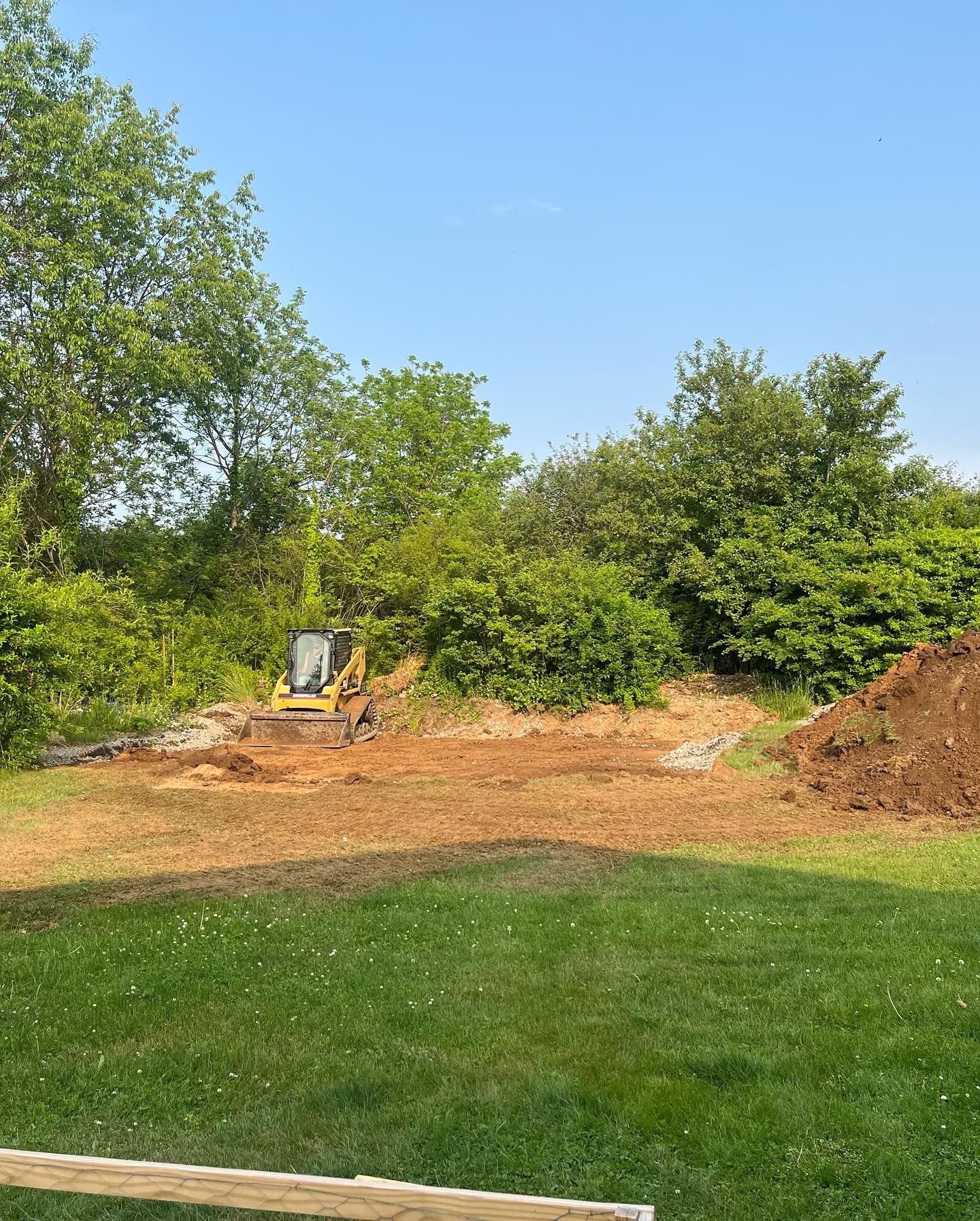 A bulldozer is moving dirt in a yard with trees in the background.