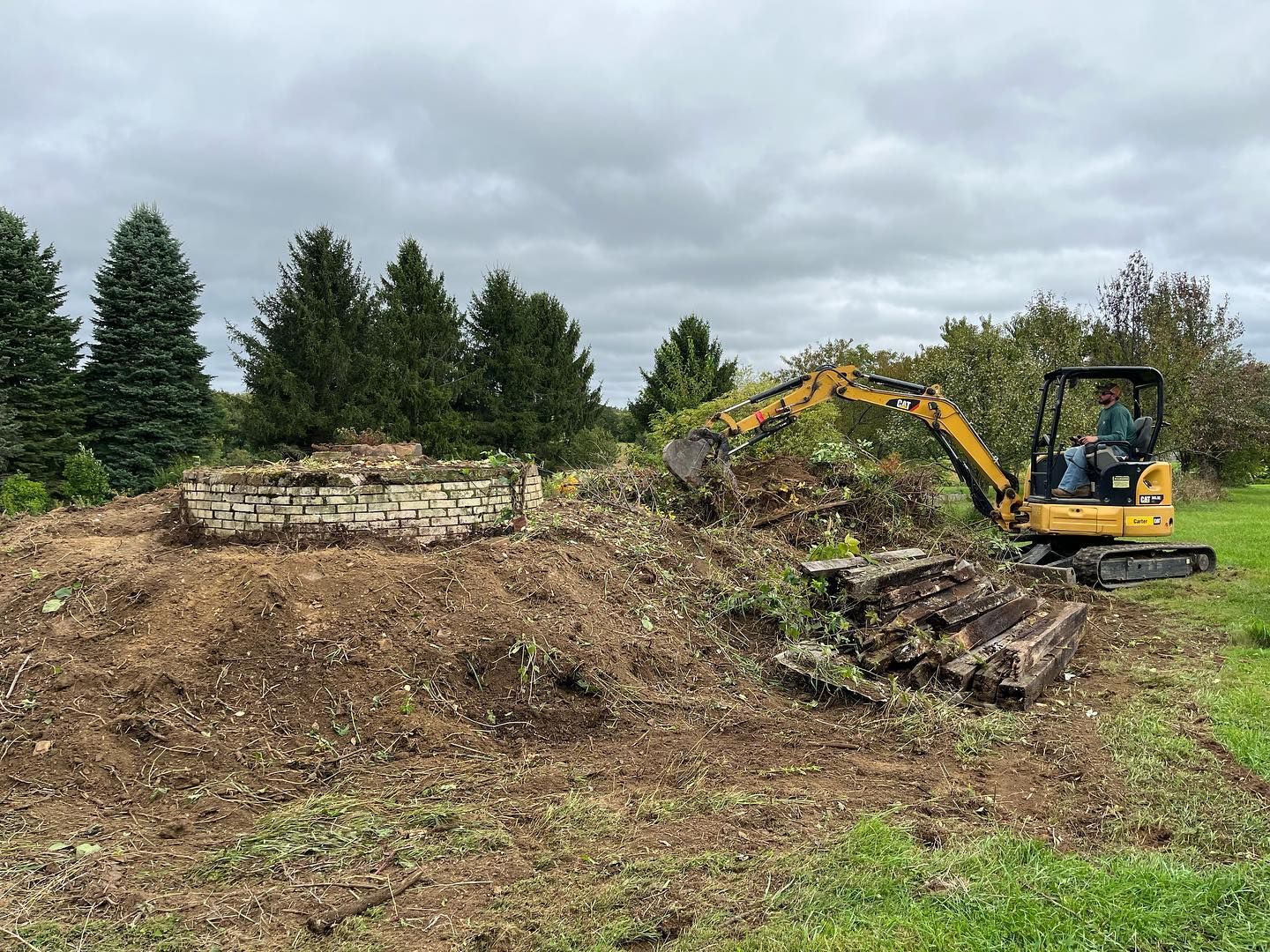A small excavator is working on a pile of dirt in a field.