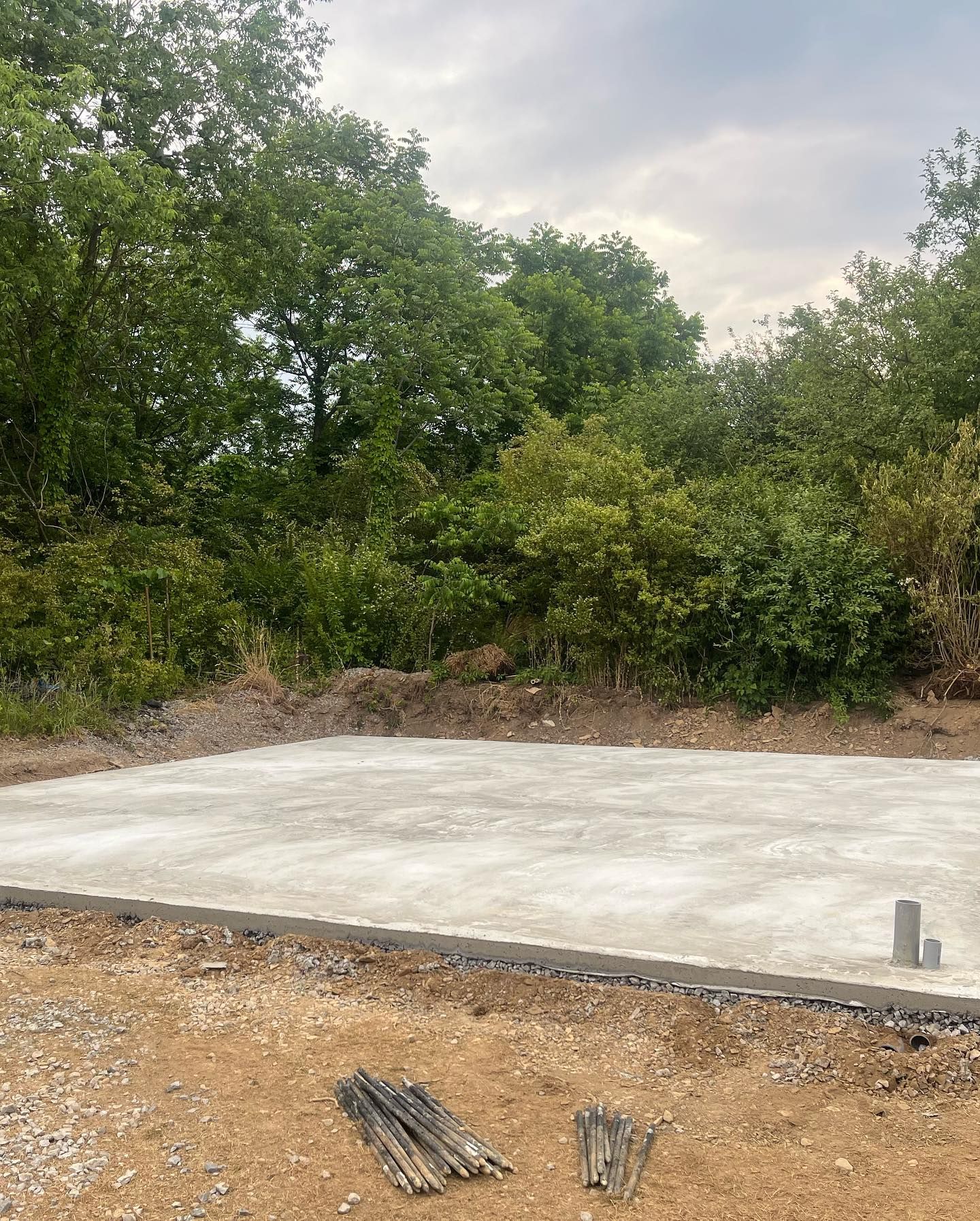 A large concrete slab is sitting in the middle of a dirt field surrounded by trees.
