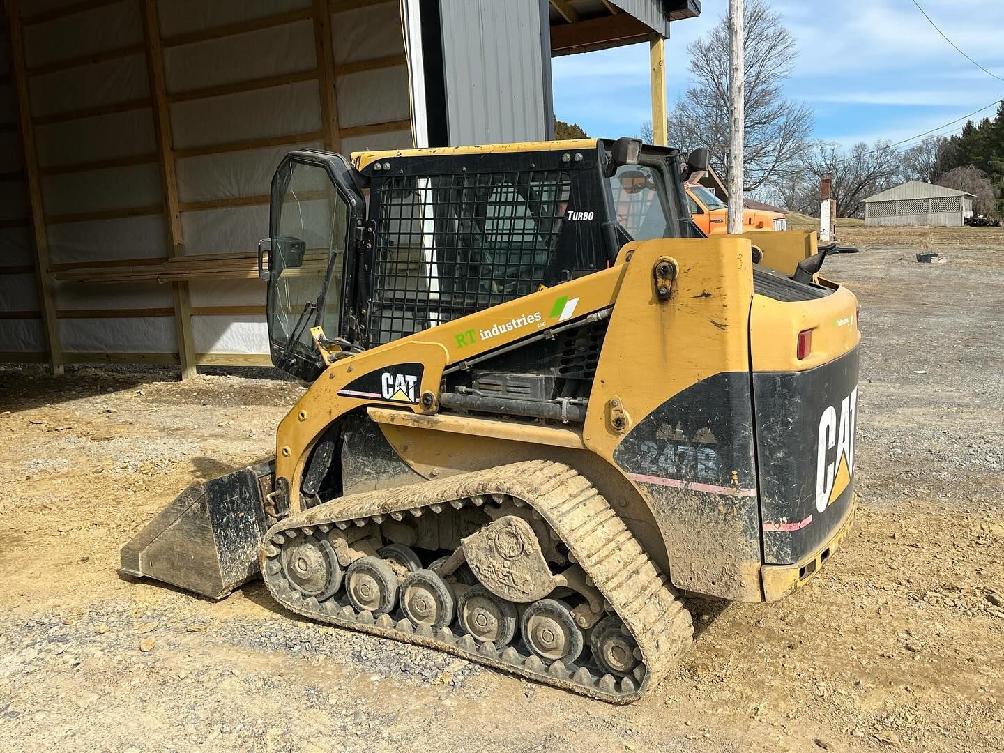 A small bulldozer is parked in a dirt lot in front of a barn.