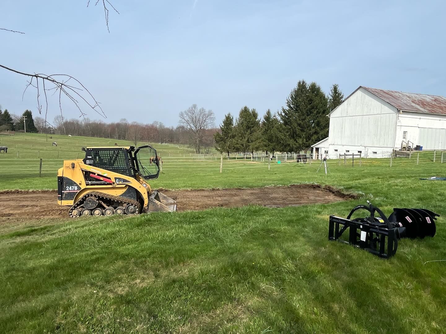 A bulldozer is moving dirt in a grassy field in front of a barn.