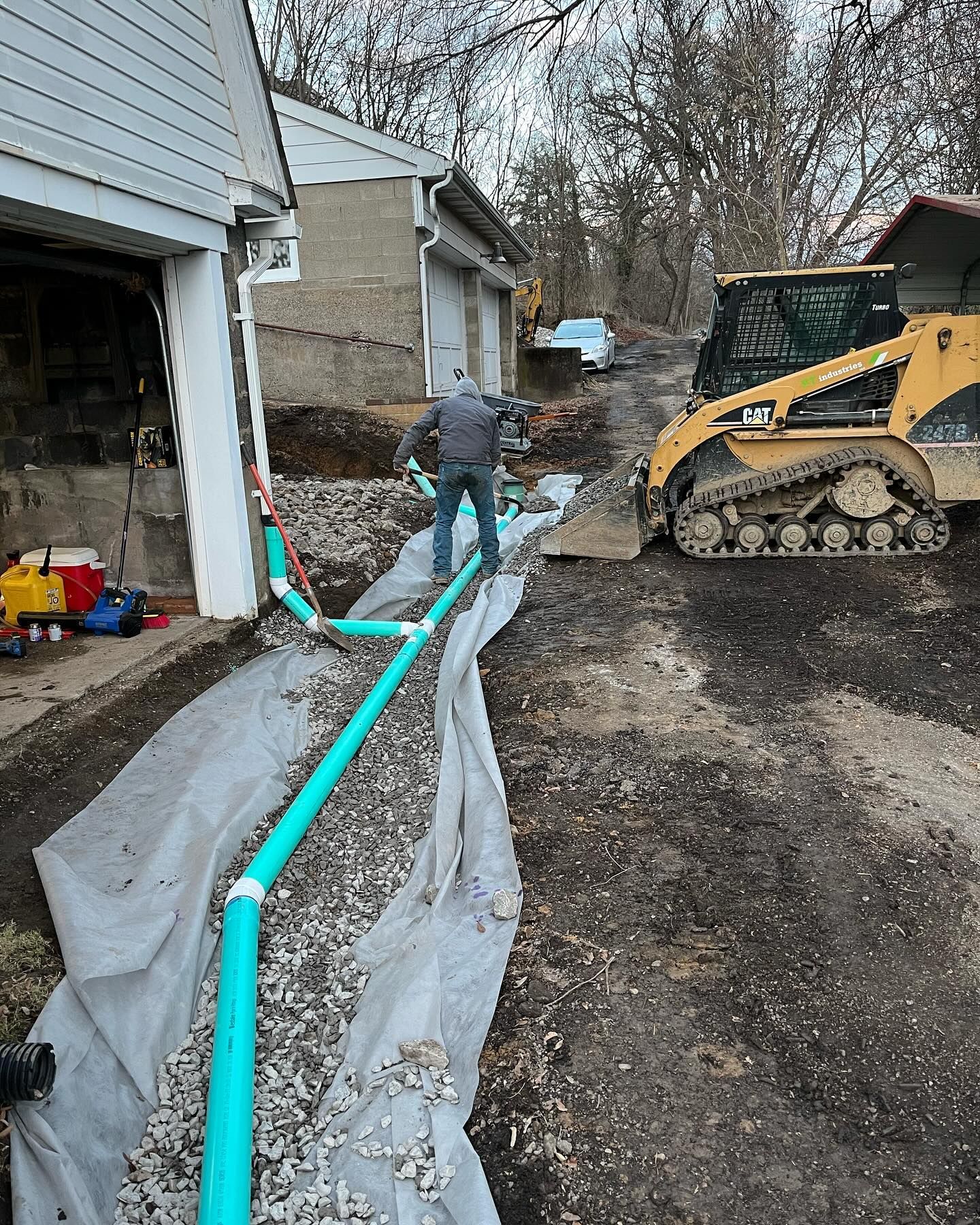 A man is working on a drainage system in a driveway next to a bulldozer.