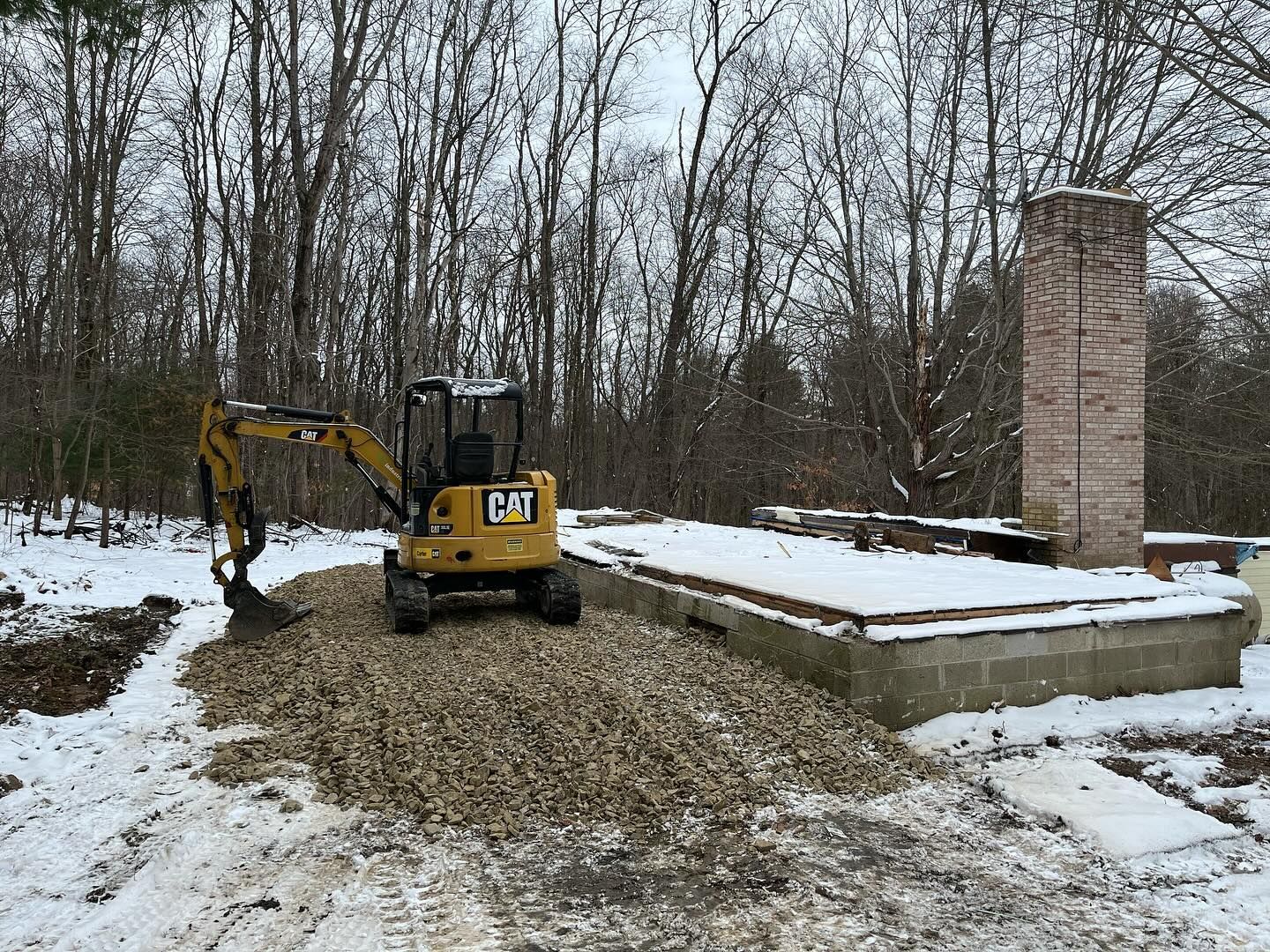A small yellow excavator is digging a hole in the snow.