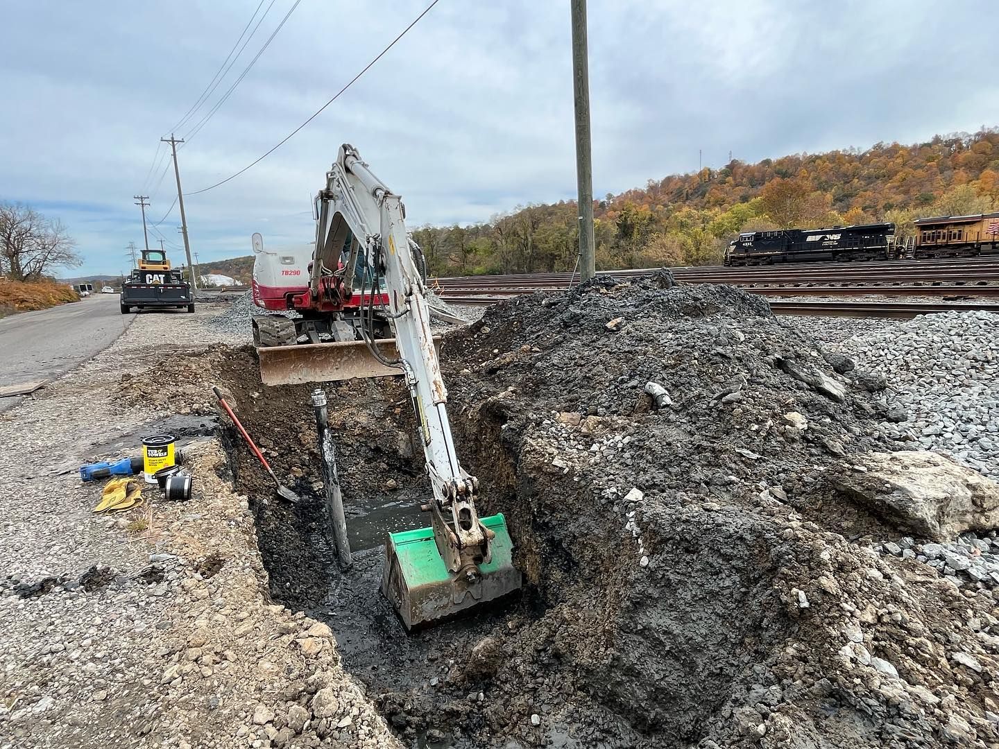 A small excavator is digging a hole in the ground next to a train track.