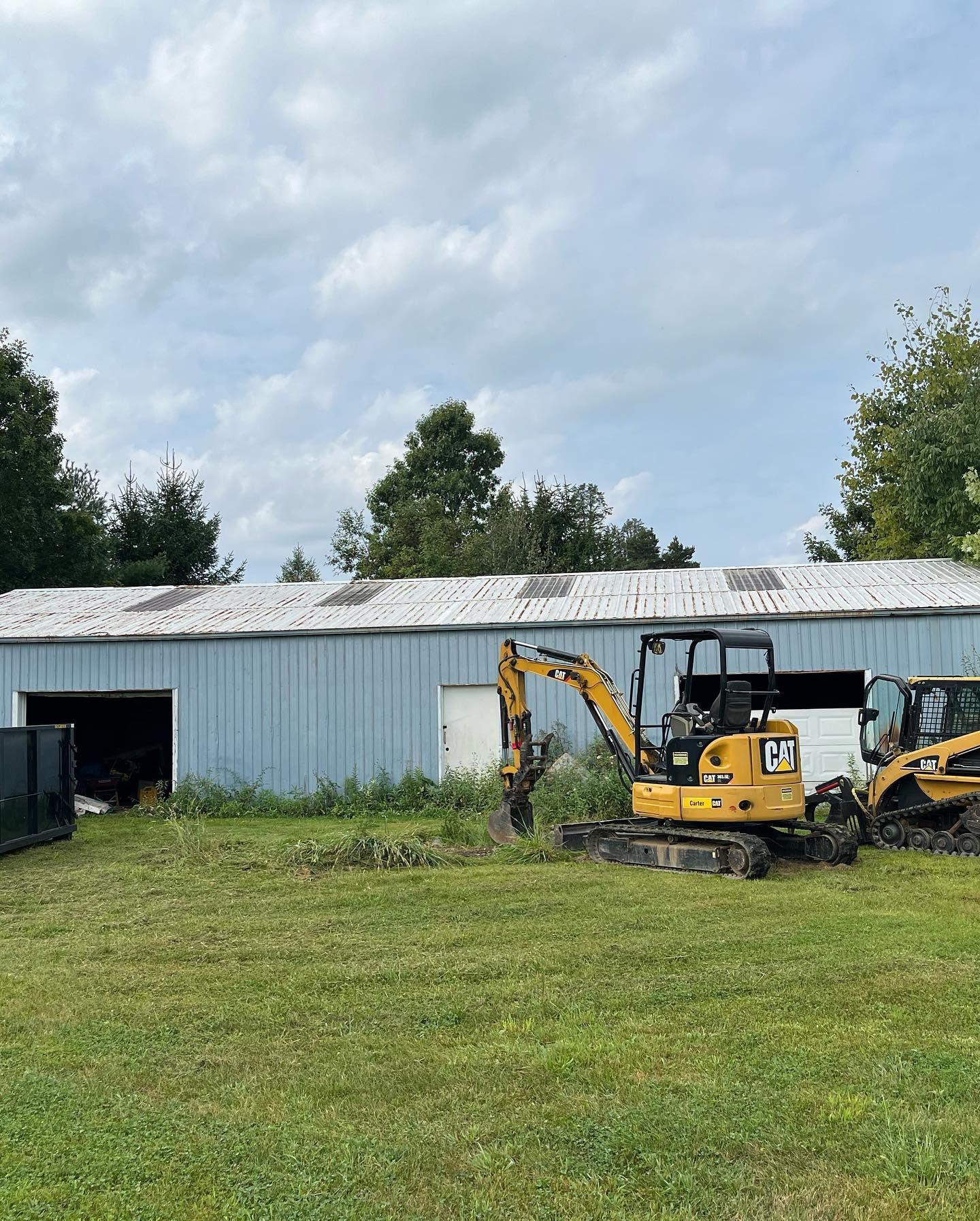 A yellow excavator is parked in a grassy field in front of a building.