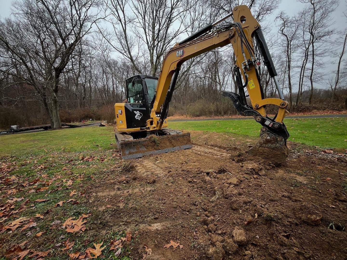 A yellow excavator is digging a hole in a field.