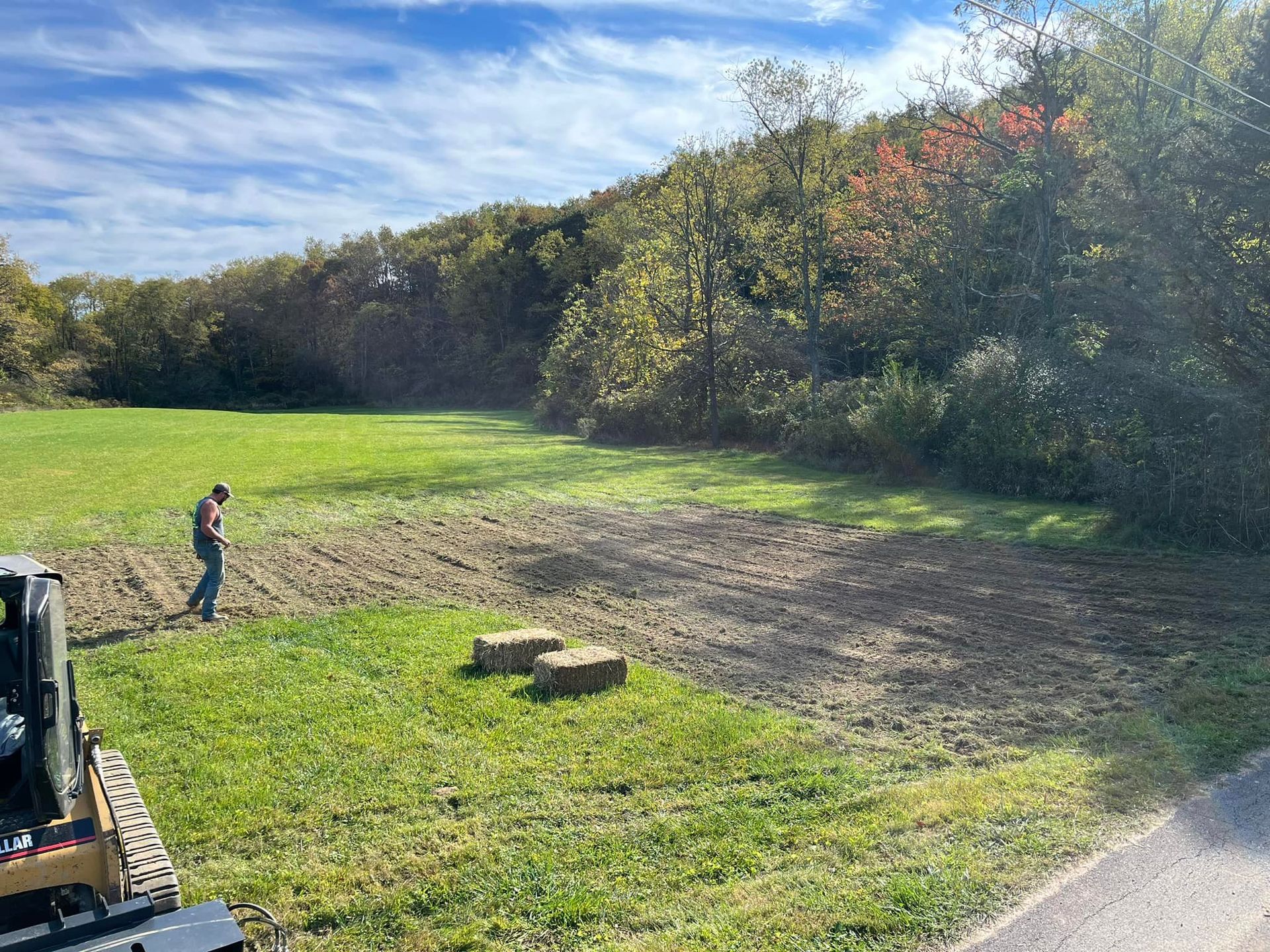 A man is standing in a field next to a bulldozer.