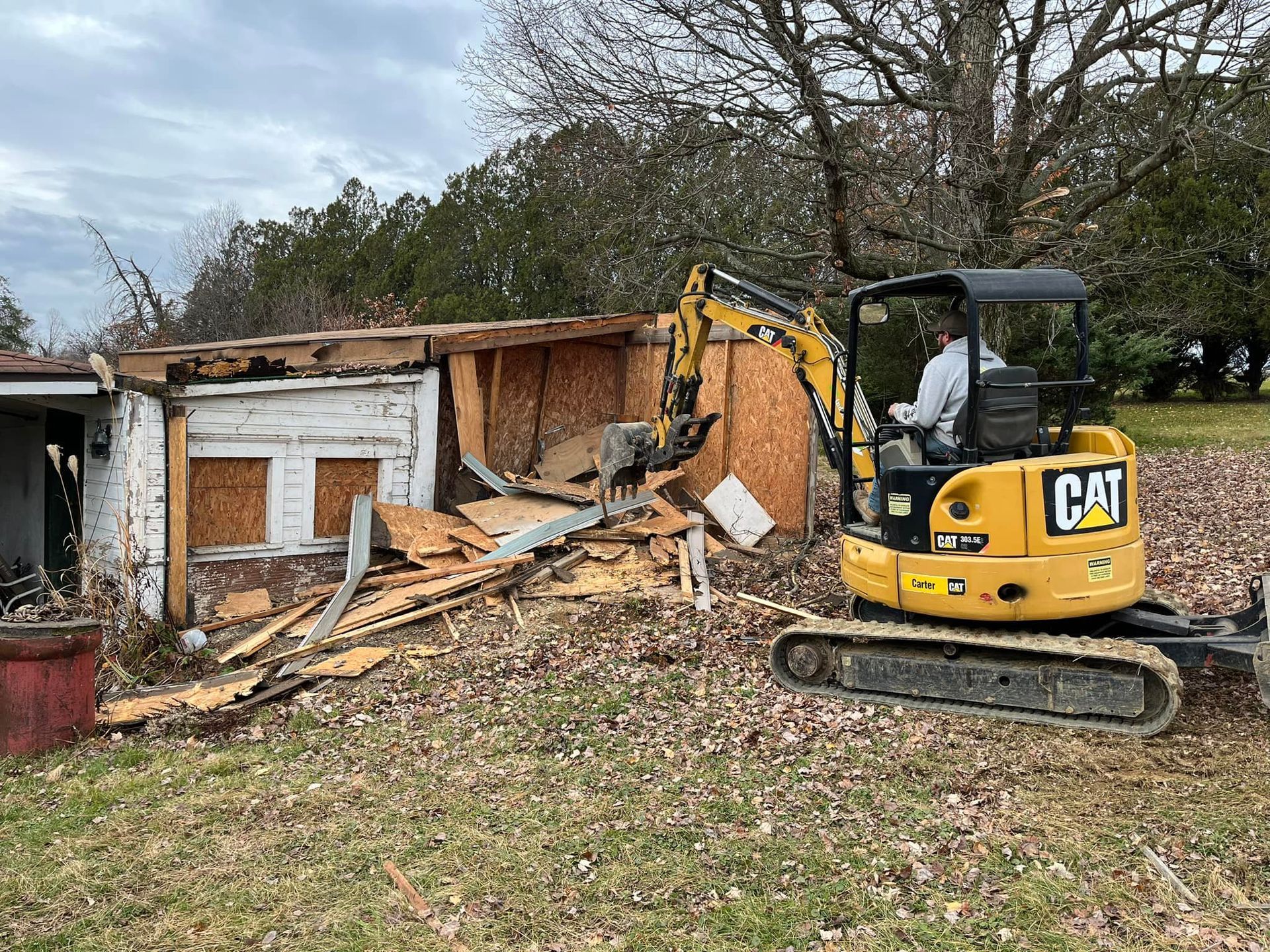 A cat excavator is demolishing a house in a field.