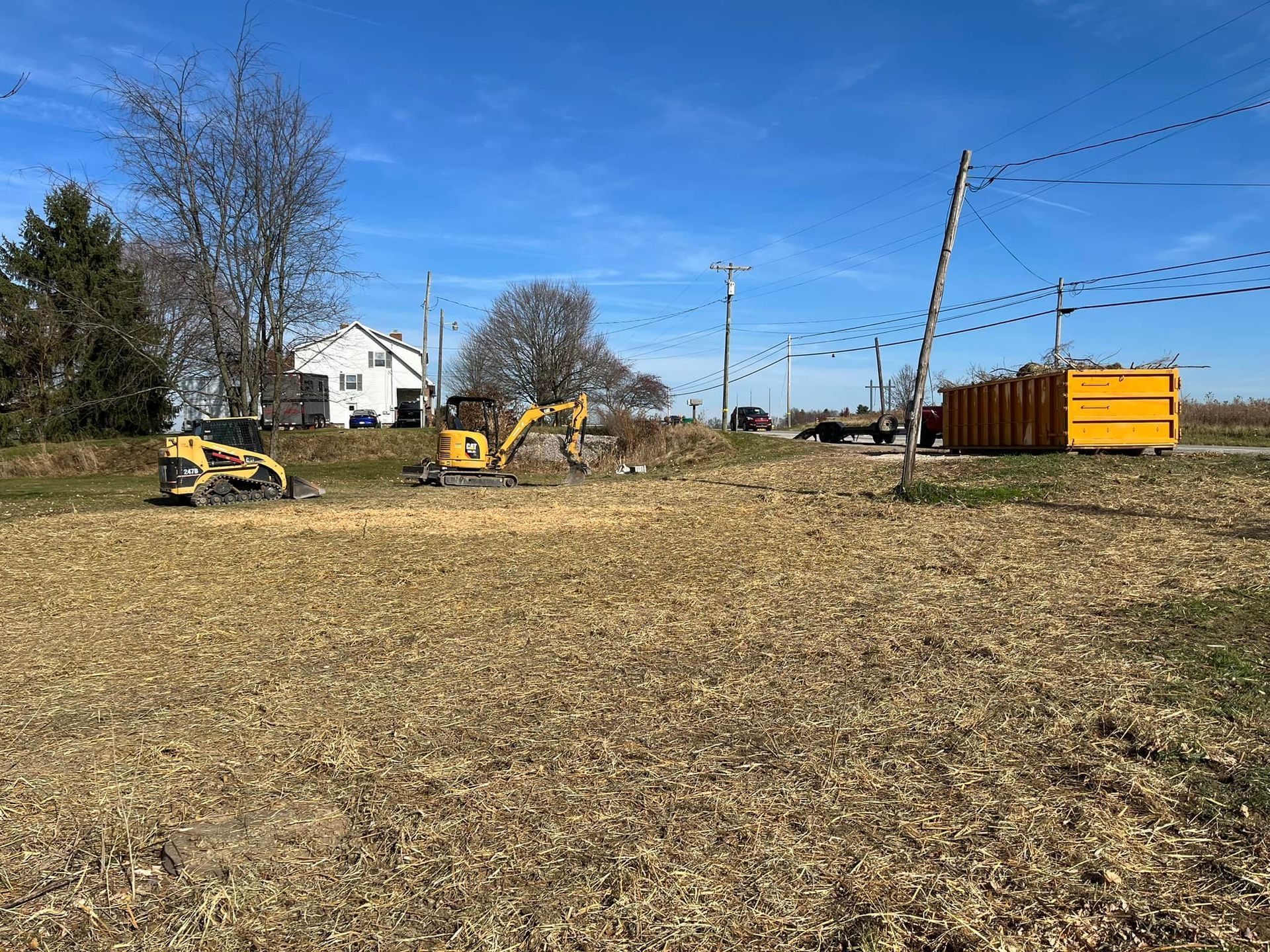 A yellow excavator is sitting in a field next to a yellow dumpster.