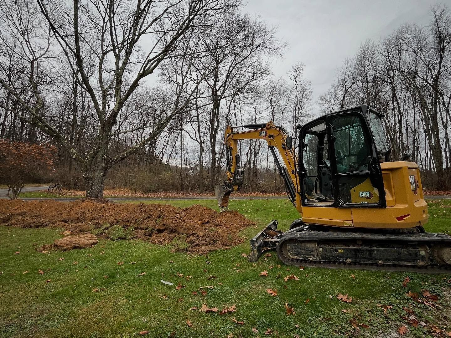 A yellow excavator is digging a hole in a grassy field.
