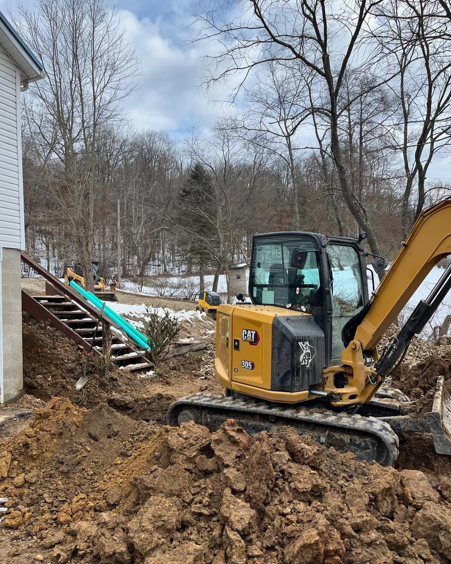 A bulldozer is digging a hole in the dirt in front of a house.