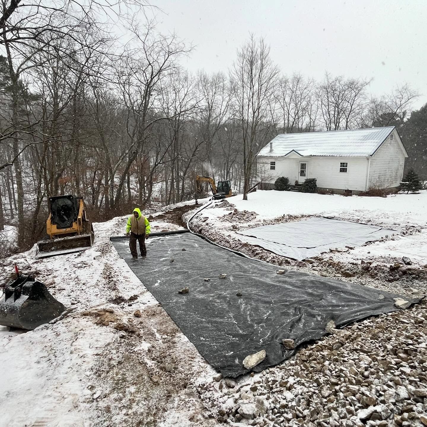 A man is standing on a snow covered road in front of a house.