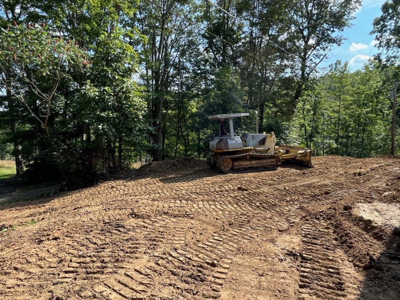 Bulldozer grading a dirt patch in a wooded area.